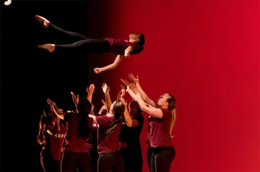 Students performing a dance routine, tossing a dancer into the air during a stage performance