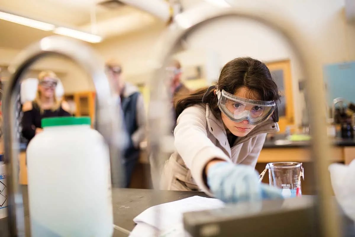 Student wearing safety goggles and gloves conducting an experiment in a science laboratory.