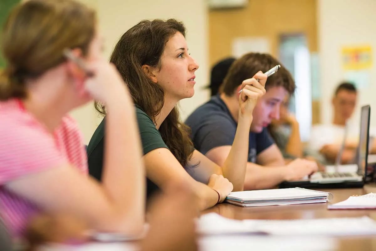 Student raising a hand and participating in a classroom discussion.