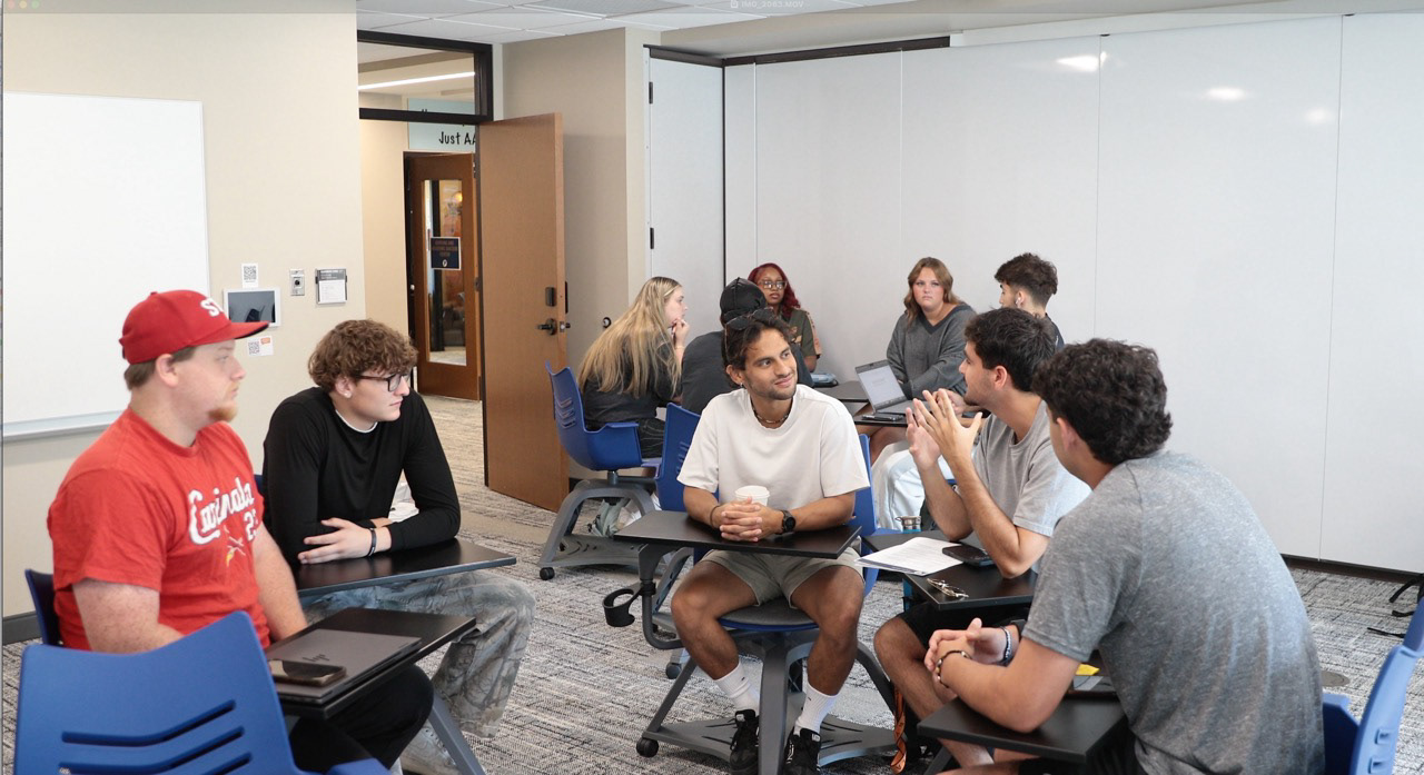 Students seated in small groups, discussing ideas during a classroom session.